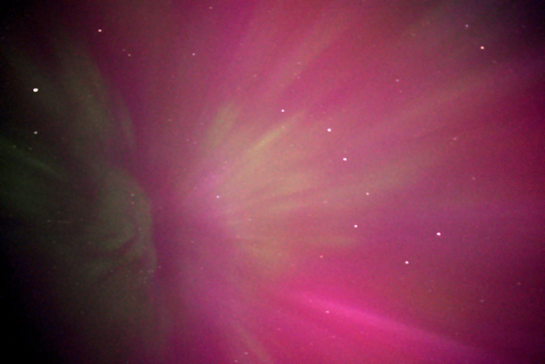 A long exposure of the aurora as seen from British Columbia, Canada. A bright pink light in the sky with streaks of green emanating from a radiant point. The big dipper/ursa major constellation can be seen on the right hand side with it's tip towards the radiant point.